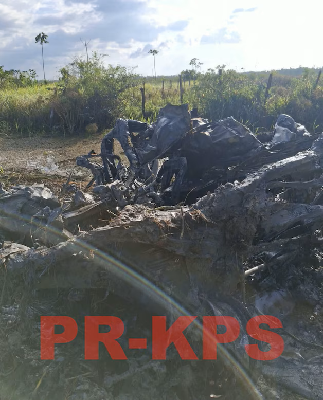 Restanten van een zwaar beschadigd, uitgebrand voertuig dat door rechercheurs wordt onderzocht in een moerasachtig gebied in Saramacca, Suriname.
