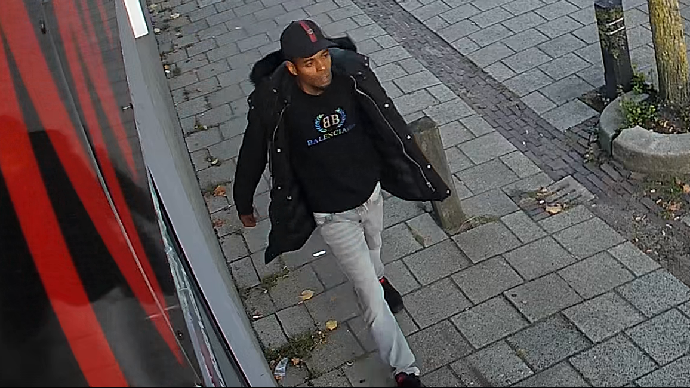 Bewakingsbeeld van de getinte verdachte in een zwarte jas met bontkraag en Balenciaga-trui.