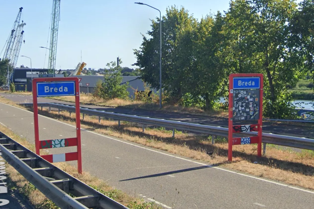 Blauw plaatsnaambord van de gemeente Breda langs de kant van de weg."