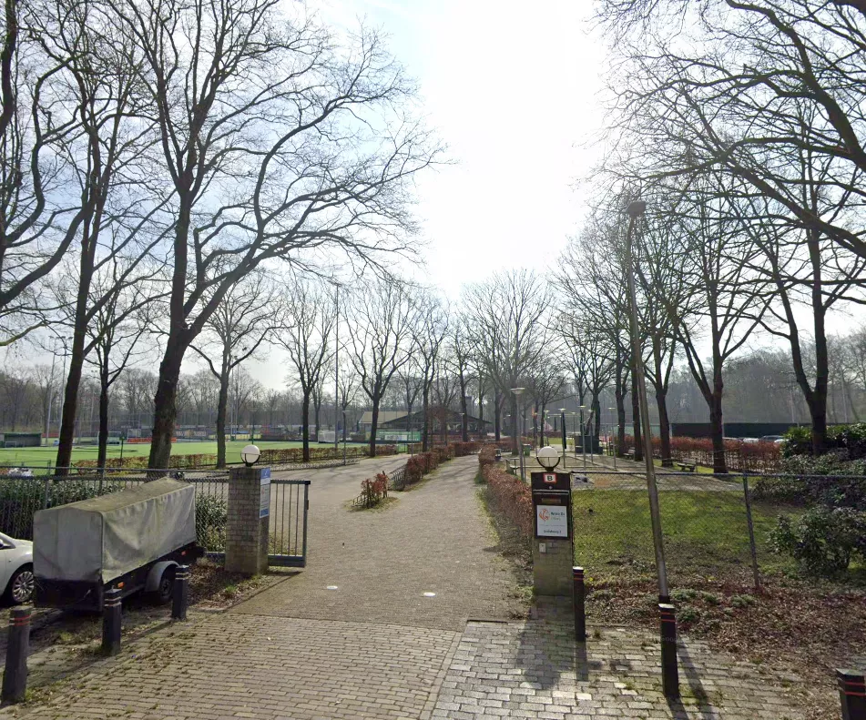 Ingang van een sportpark in Tilburg met hockeyvelden op de achtergrond.