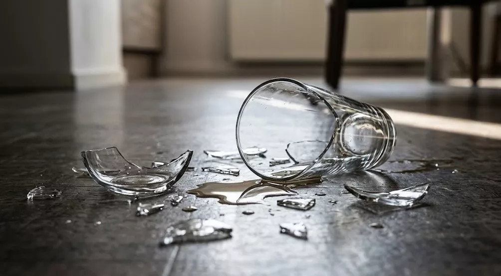 Een gebroken drinkglas op de grond, symbool voor de zware mishandeling waarbij een vrouw blijvend gezichtsletsel opliep.